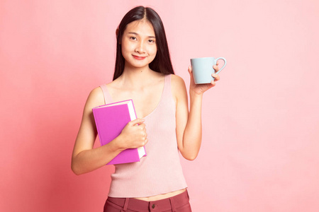 年轻的亚洲女人，带着一本书和一杯粉红色背景的咖啡
