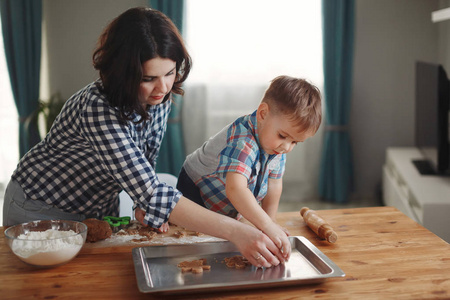 母亲和儿子穿着格子衬衫，在厨房里煮面粉和面团