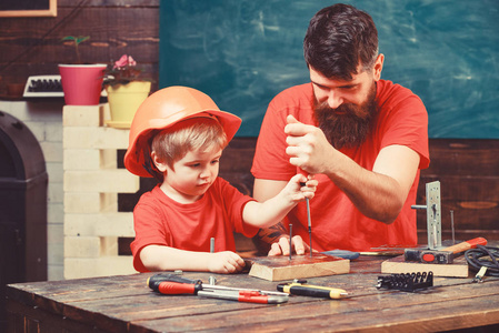 团队合作的工作理念。父亲, 家长用胡子教小儿子用工具螺丝刀。男孩, 孩子忙于防护头盔学习使用螺丝刀与爸爸