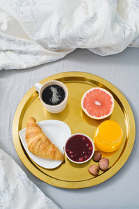 早餐在床上酒店服务。 咖啡果酱牛角面包橙汁葡萄柚荔枝。 顶视灯背景