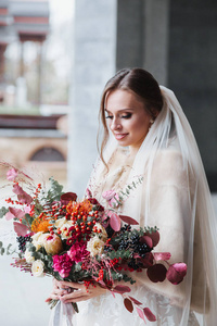 年轻美丽的新娘与婚礼花束寻找户外的一面