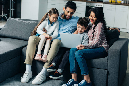 快乐的西班牙裔家庭坐在沙发上，看着家里的笔记本电脑