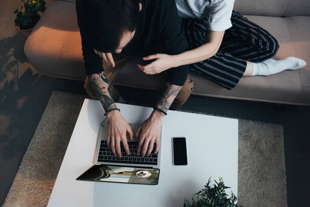 在家中使用笔记本电脑并在屏幕上显示预订网站时，夫妇坐着拥抱的裁剪视图