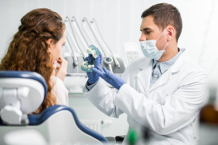 牙医在乳胶手套中的选择性聚焦，显示女性患者附近的牙齿模型