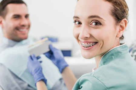 有选择的焦点，开朗的牙医，牙套，微笑，同时保持调色板附近的病人。