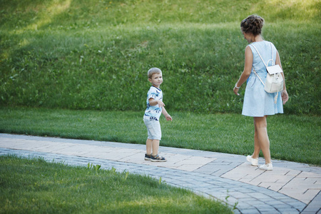 母亲穿着蓝色的衣服，金发男孩走在公园绿色草地上的石头路面上