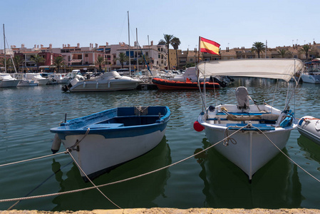 夏天，小渔船停泊在西班牙南部的港口墙上。 西班牙国旗可以在背景中看到