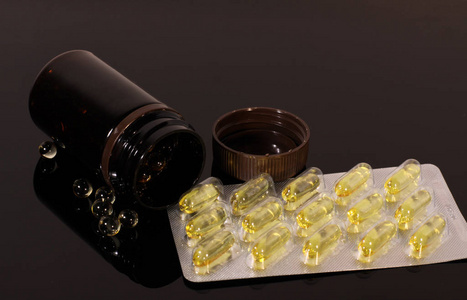 药片鱼油胶囊和一罐装在黑色镜子桌上的药片