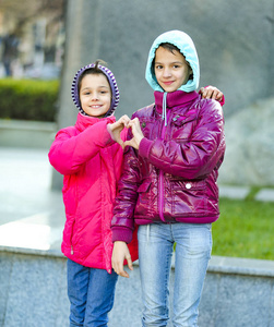 这两个穿着温暖夹克的快乐女孩在秋天的城市的石墙背景上展示了心灵的象征