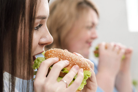 两个女孩, 身材苗条, 胖胖的, 金发碧眼的, 黑发的, 吃汉堡包。在白色背景下, 饮食和适当营养的主题