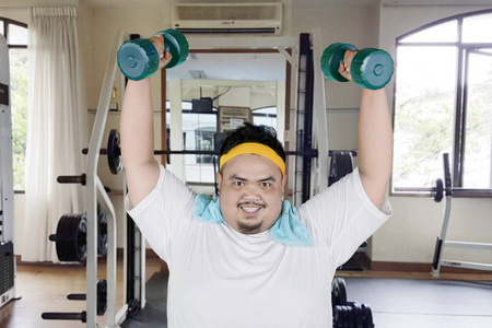 在健身房锻炼时，快乐的肥胖男子举起两个哑铃