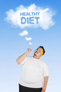 一个年轻的胖子站在蓝天下，把健康饮食文字指向云端