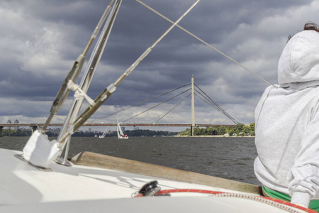 一个穿着白色夹克的女孩坐在游艇上。 在河岸桥前面
