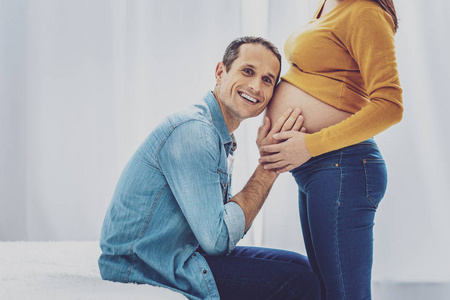 高兴的男人把头放在妻子的肚子上