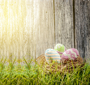 五颜六色的复活节彩蛋在绿草上的巢里，有阳光和木制栅栏的背景。 快乐的复活节