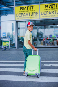 可爱的小男孩与大绿色手提箱在国际机场飞行前