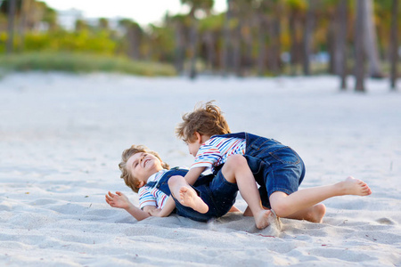 两个小男孩在热带海滩上玩的开心, 快乐的最好的朋友玩, 友谊的概念。兄弟姐妹兄弟, 双胞胎战斗, 跑和跳跃在家庭看与棕榈树在背景