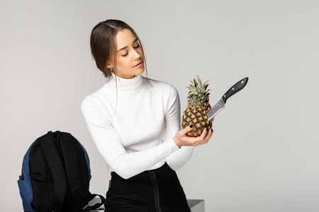 时髦的年轻女孩拿着菠萝在她的手与刀