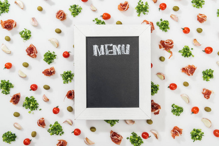 粉笔板的顶部视图，菜单字母在意大利火腿橄榄大蒜丁香和樱桃番茄中。