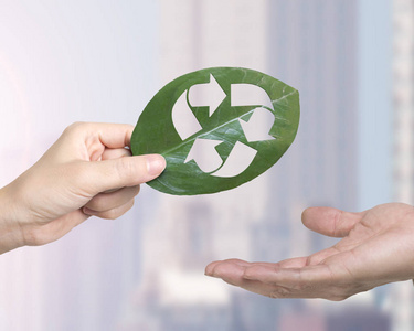 提供资源回收零浪费和绿色友好技术的概念，女性手给男性手一片带有回收符号孔的叶子。