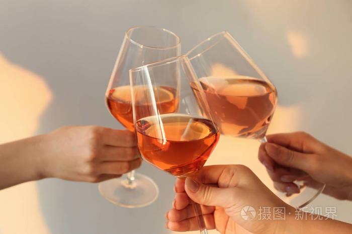 女人用淡色背景下的美味葡萄酒碰杯