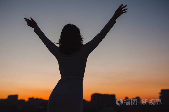 城市夕阳中举手的幸福女人的剪影