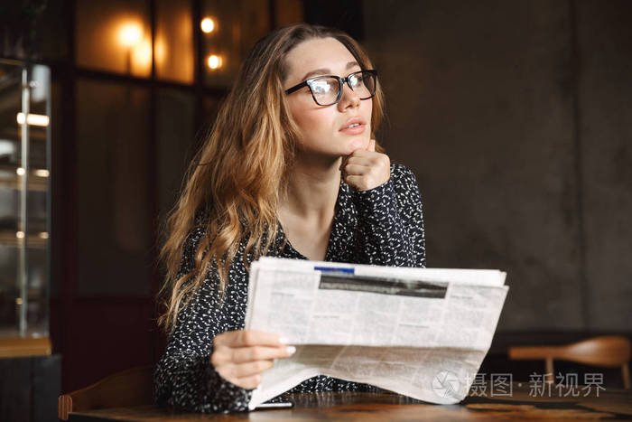一个思考的美丽的年轻女人坐在咖啡馆室内阅读报纸的形象.