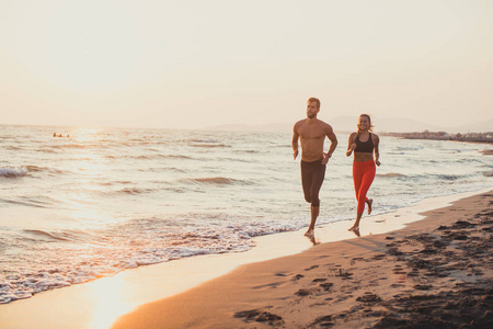英俊的白种人男人和美丽的女人在日落时在沙滩上奔跑。