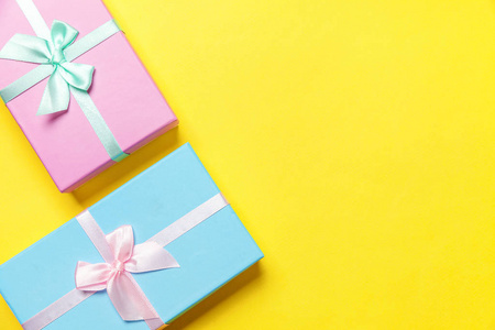圣诞节新年生日情人节庆祝礼物浪漫的概念。 礼品盒包装蓝色粉红纸隔离在黄色色彩鲜艳的现代时尚背景上。 平躺顶视复印空间