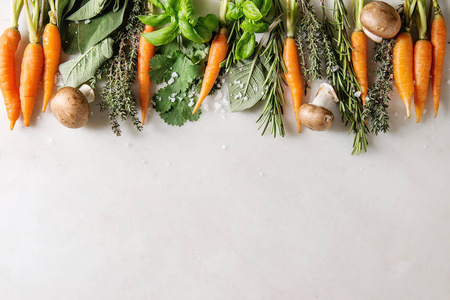 各种新鲜的厨房草药与迷你胡萝卜和香菜蘑菇在白色大理石背景上排。 平坦的铺设空间。 烹饪概念食品背景。