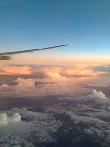从飞机的窗户到机翼的景色和云层上方美丽的日落。 蓝天，有不同类型的云被夕阳照亮。 垂直照片。