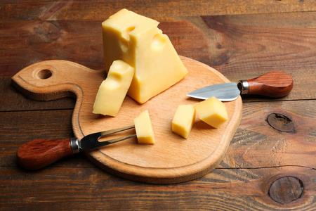 硬切片黄色马斯达姆奶酪刀和叉子奶酪在切割板上的木制背景。 奶酪的概念。