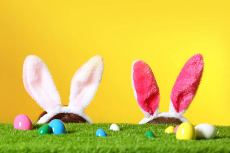 绿色草坪上的复活节彩蛋和戴着带兔子耳朵的头巾的小女孩
