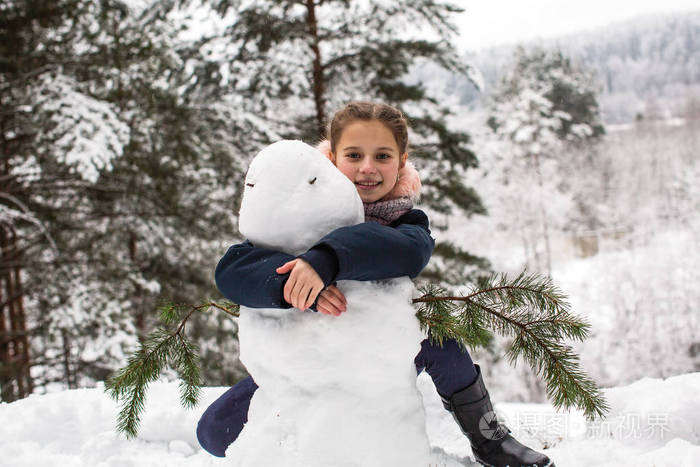 小女孩在冬天下雪的公园里堆雪人.