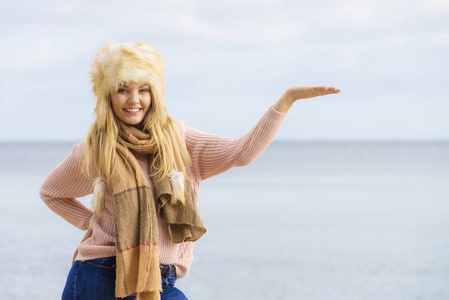 十几岁的女性在秋天的天气里花时间在海滩上，指着复制空间。 戴着毛衣围巾和毛皮帽。
