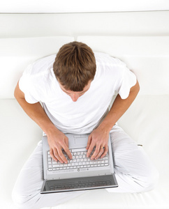一个年轻人休闲沙发同时使用一台笔记本电脑上的肖像