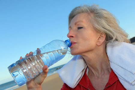 从瓶在海滩活动高级女人饮用水