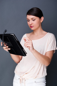 年轻漂亮的女人举行平板电脑和眼镜微笑灰色背景上的肖像