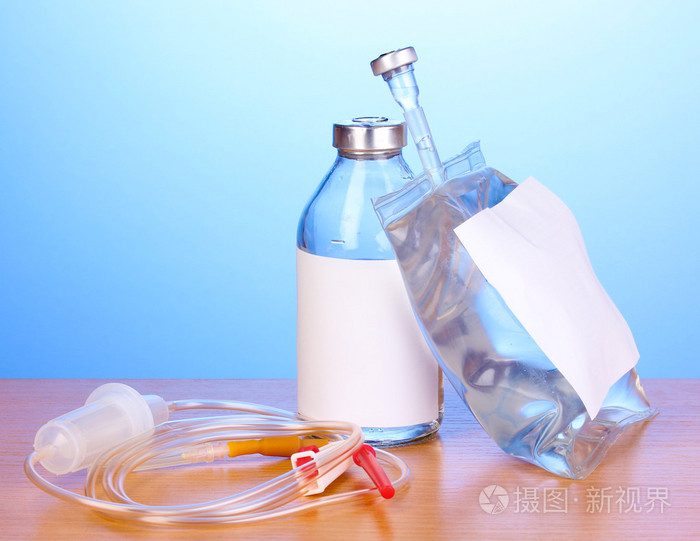 瓶和静脉注射抗生素和设置在蓝色背景上的木桌上的塑料输液袋