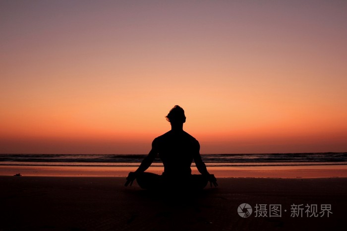 在日落的海边背景上的瑜伽姿势的男人剪影.冥想