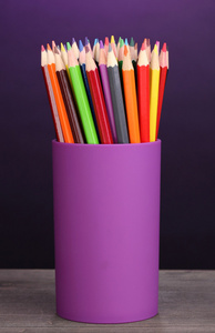 在紫罗兰色的背景上的木桌上的玻璃颜色铅笔