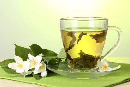 杯绿茶与绿色背景上的木桌上的茉莉花