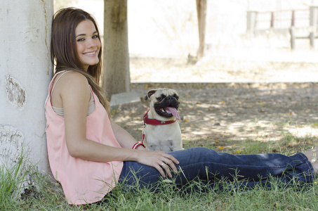 可爱的年轻女子，与她的八哥犬狗坐在旁边一棵树