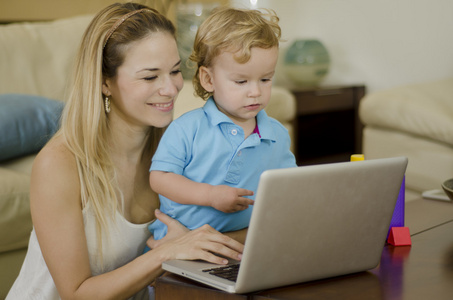 年轻美丽的母亲与她的儿子一起使用一台笔记本电脑