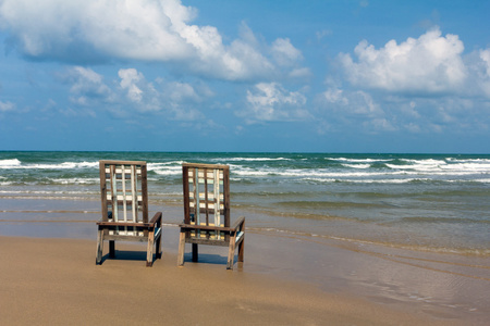 热带海滩上的两个木制帆布椅子。