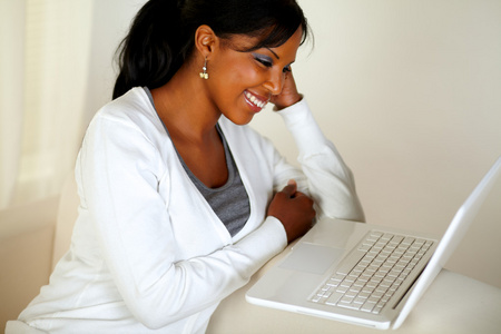 微笑着的年轻女子在便携式计算机屏幕上阅读