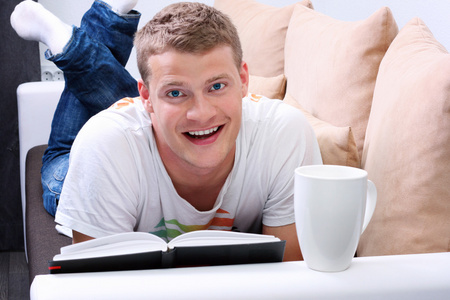 笑的年轻人读一本书，在沙发上放松