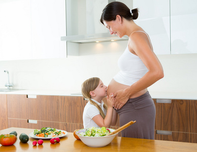 美丽的怀孕母亲与她的女儿在厨房
