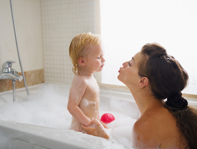在充满泡沫的浴缸接吻清洗时母亲的婴儿