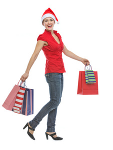 快乐的年轻女人在圣诞帽子带着购物袋行走